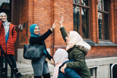Happy female muslim friends giving high-five against building