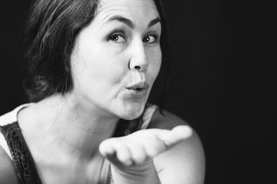 Close-up portrait of woman blowing kiss against black background