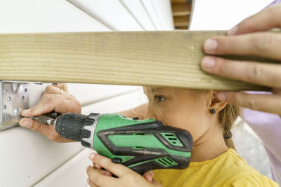 Girl installing bracket on wooden wall with father outside house