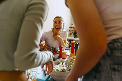 Cheerful young woman enjoying lunch with female friends at home
