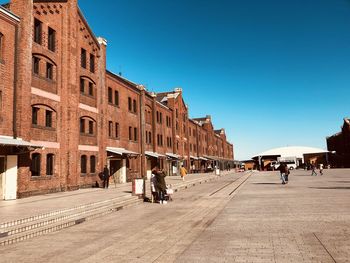 People on street amidst buildings against clear blue sky