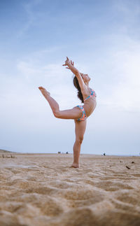 Full length of woman jumping at beach against sky