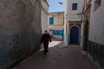 Rear view of man walking on footpath amidst buildings
