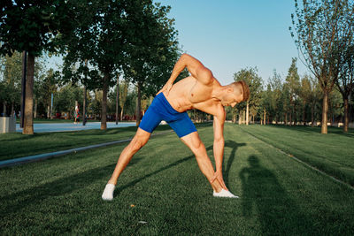 Full length of shirtless man sitting on grass