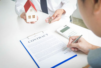 Midsection of real estate agent giving keys while client signing contract 