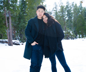 Portrait of young couple standing on snow covered land against trees