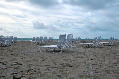 Empty chairs on beach against sky