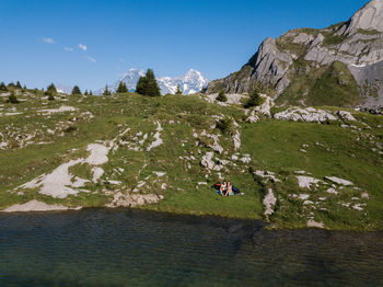 Scenic view of landscape with man and woman sitting on grass against sky