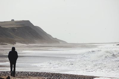 Rear view of man walking at beach against clear sky