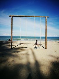 Girl on swing at beach against sky