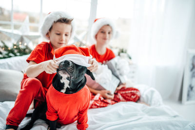 Smiling kids with gift box sitting with dog on bed at home