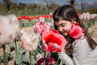 Close up view of girl in white dress watching big flower sitting in tulip field