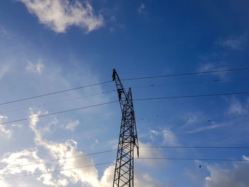 Low angle view of silhouette electricity pylon against blue sky