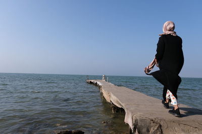 Rear view of woman by sea against clear sky