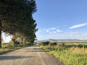 Empty road amidst field against sky