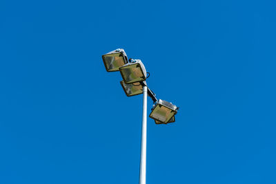 Low angle view of floodlights at a sports ground against blue sky