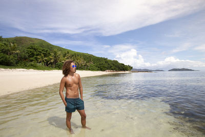 Full length of shirtless man standing at beach against sky