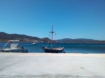 Boats moored at calm sea against clear blue sky