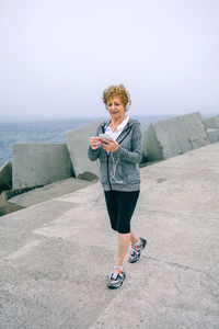 Full length of woman listening music while walking on promenade against sky