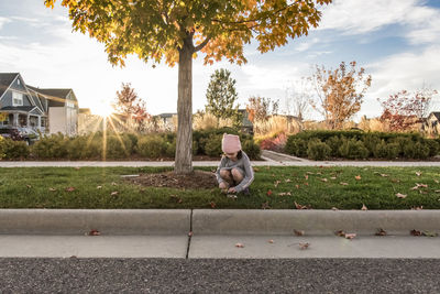 Girl playing while crouching by road on grass in city