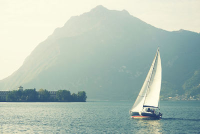 Sailboat sailing on sea against mountains