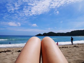 Low section of woman on beach against sky