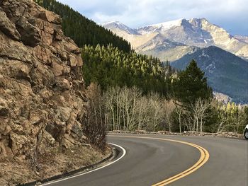 Road amidst trees and mountains against sky