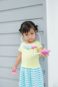 Portrait of girl showing toy stethoscope while standing against wall
