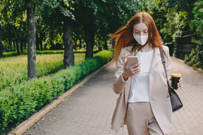 Redhead woman wearing face mask for virus protection. young business woman with cell phone in hand