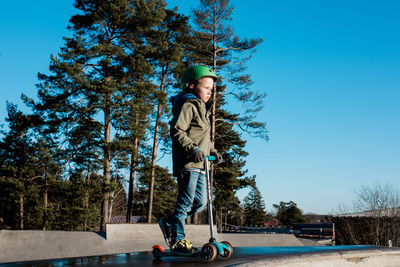 Boy standing on his scooter at a skatepark in the sunshine