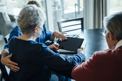 Home caregiver discussing over tablet computer with senior couple while sitting at dining table