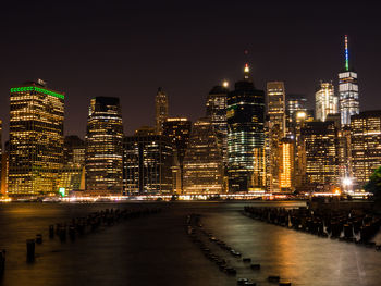 Illuminated city by river against sky at night