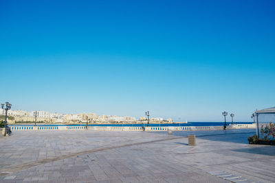 Promenade by sea against clear blue sky