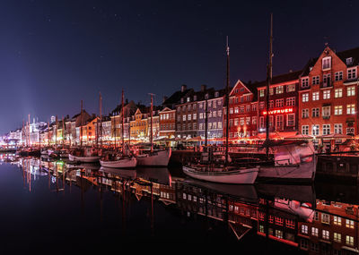 Boats moored in harbor against buildings at night