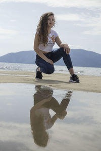 Full length of young woman sitting on shore against sky