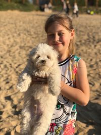 Portrait of smiling girl holding white dog at beach