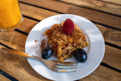 A delicious-looking slice of orange cake sits on a white plate, adorned with a raspberry