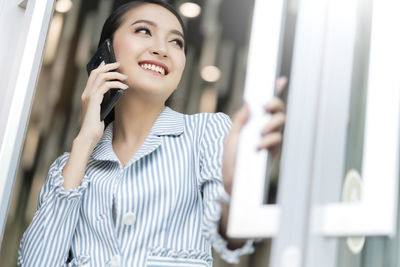 Smiling young woman looking away while standing on mobile phone