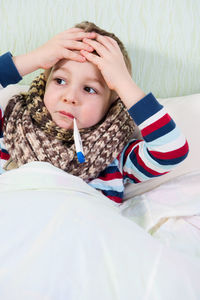 Cute boy holding thermometer in mouth at home