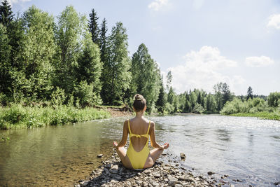 Woman meditating sitting at riverbank on sunny day