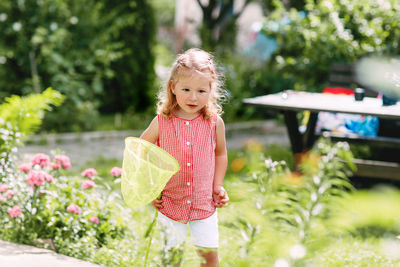 A little girl with a net in her hand plays in the garden and catches moths