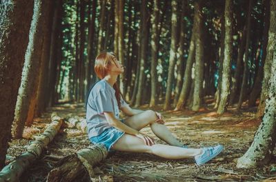 Side view of woman sitting on fallen tree trunk in forest