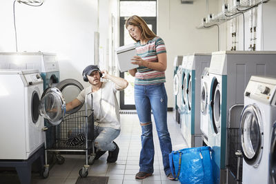 Confused university student showing detergent pack to male friend at laundromat