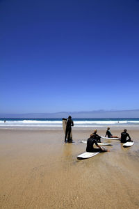 Surfers with surfboard on shore at beach against clear blue sky