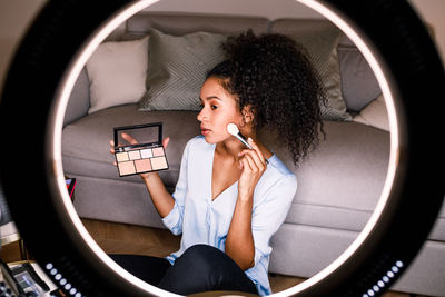 Woman applying face powder seen through lens at home