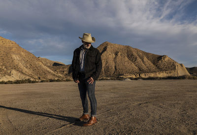 Adult man in cowboy hat standing against mountains in tabernas desert. almeria, spain