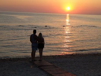 Rear view of couple standing at beach during sunset