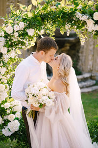 Couple kissing while holding bouquet outdoors