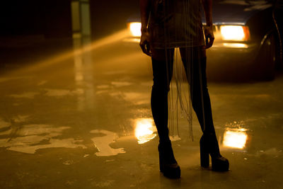 Low section of woman in high heels standing on illuminated street at night