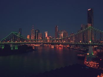 Illuminated buildings by river against sky at night